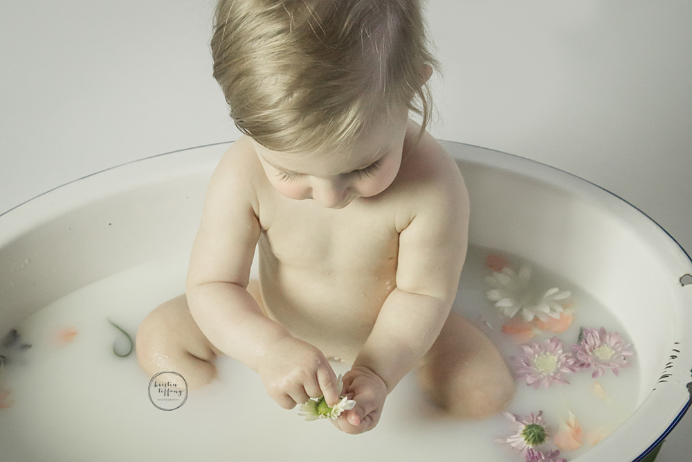 a photo of a baby girl in a floral milk bath