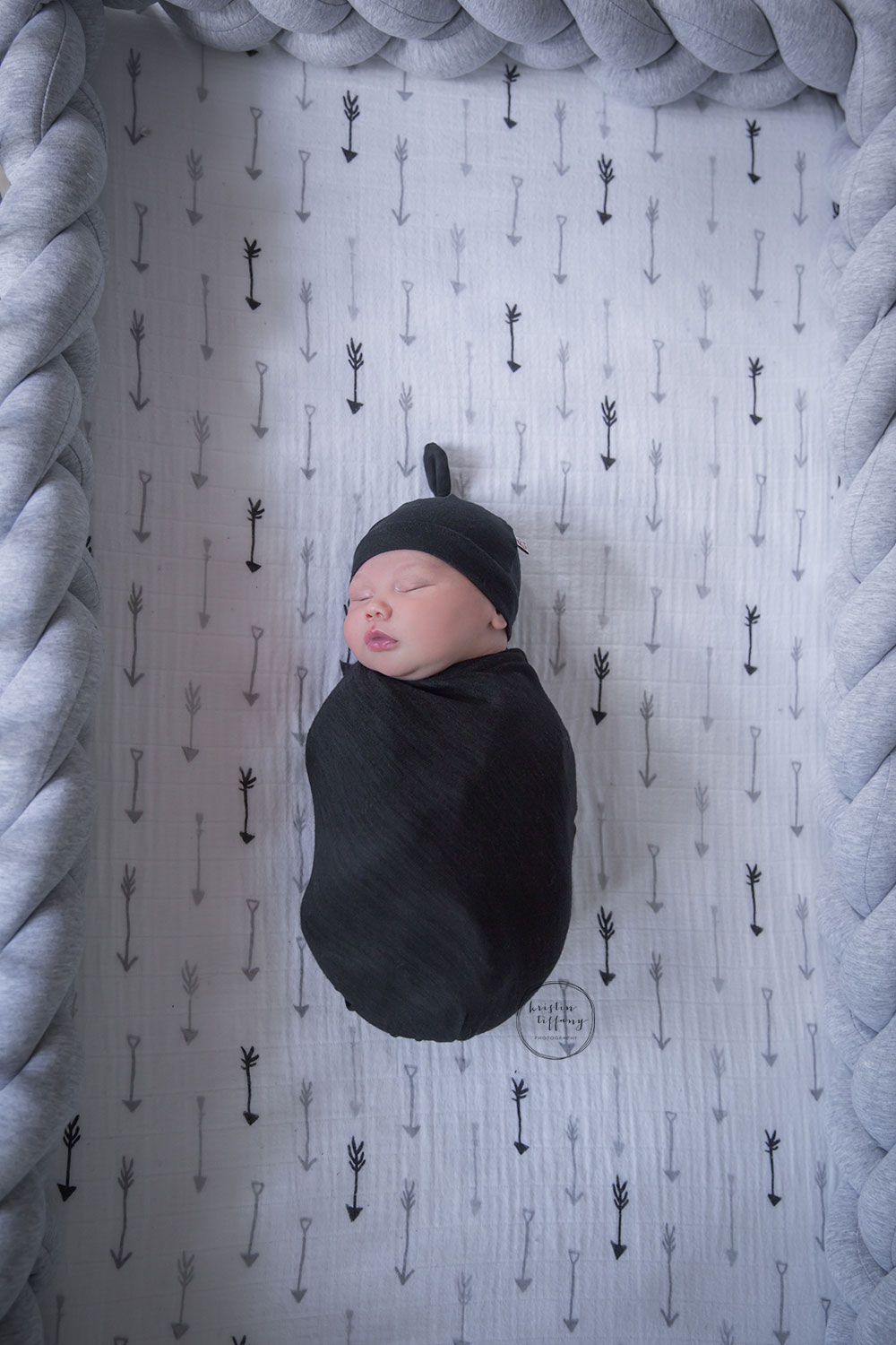 a photo of a newborn baby sleeping in his crib swaddled in a hat