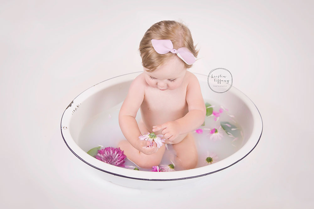 a photo of a baby girl in a floral milk bath