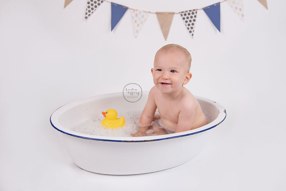 a photo of a baby boy having a bubble bath in an old wash basin