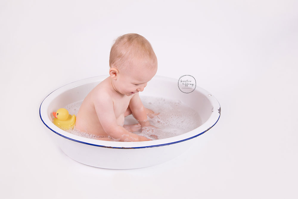 a photo of a baby boy having a bubble bath in an old wash basin