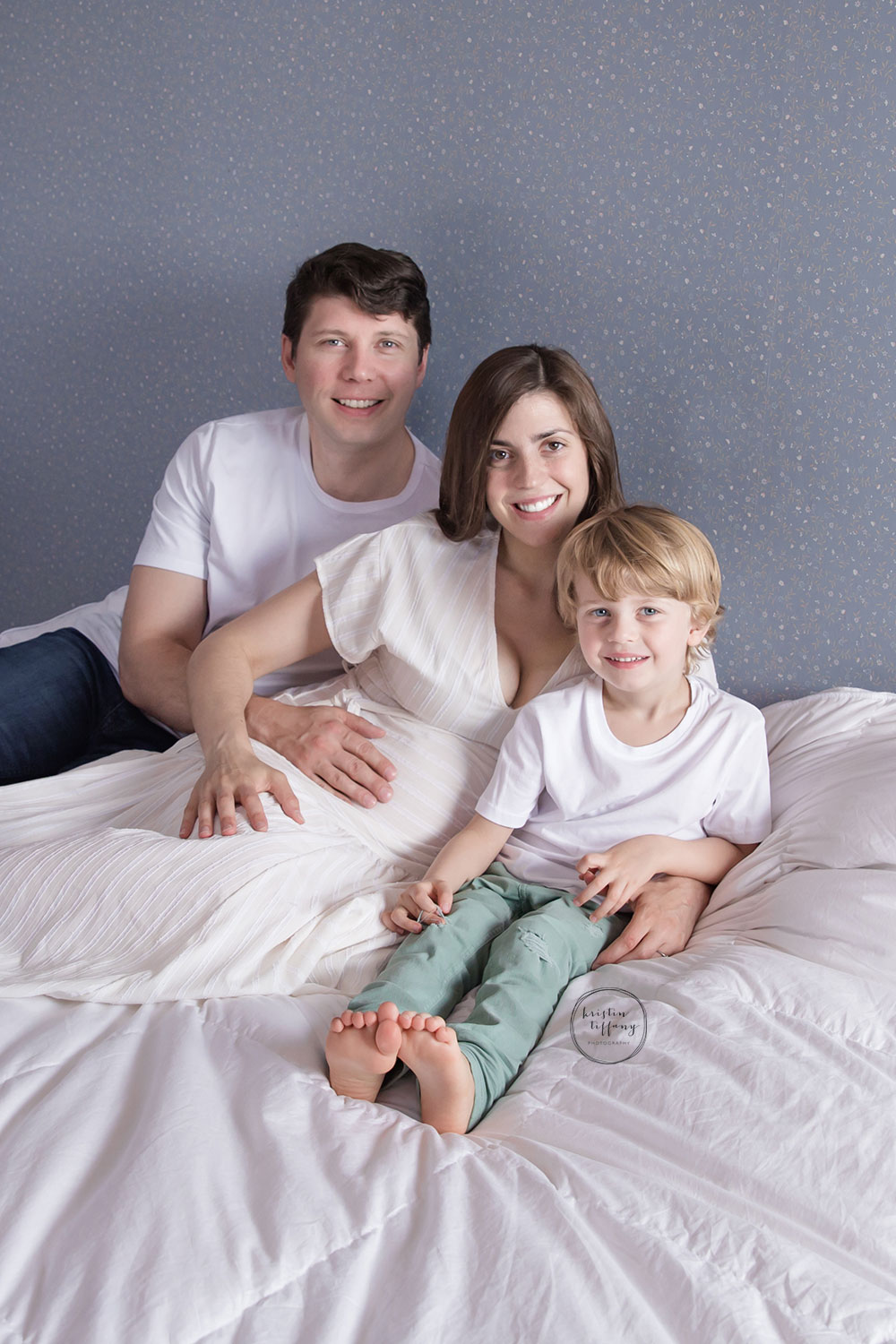 a maternity photo of a family laying on a white duvet