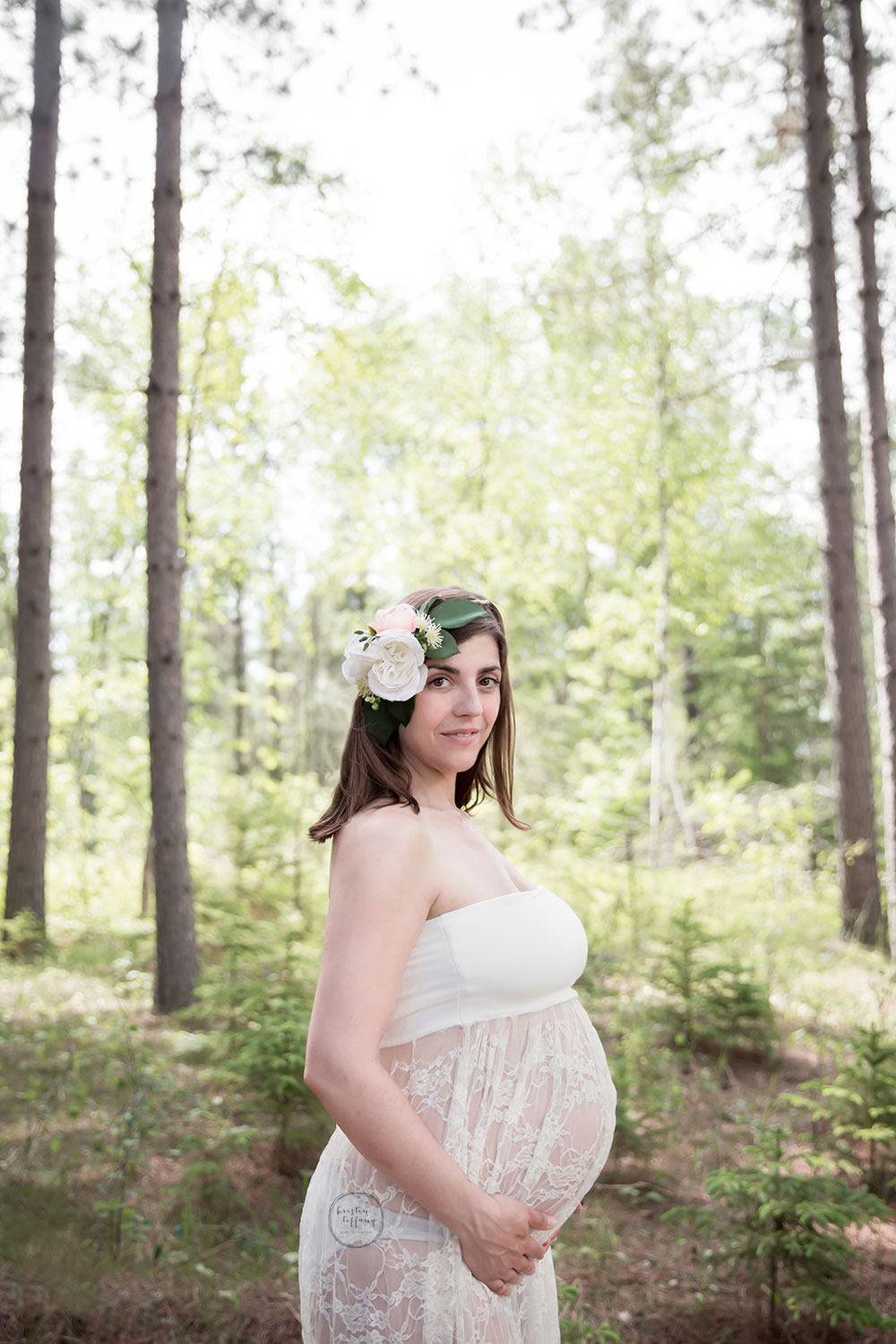 a maternity photo of a woman wearing a lace gown in the forest