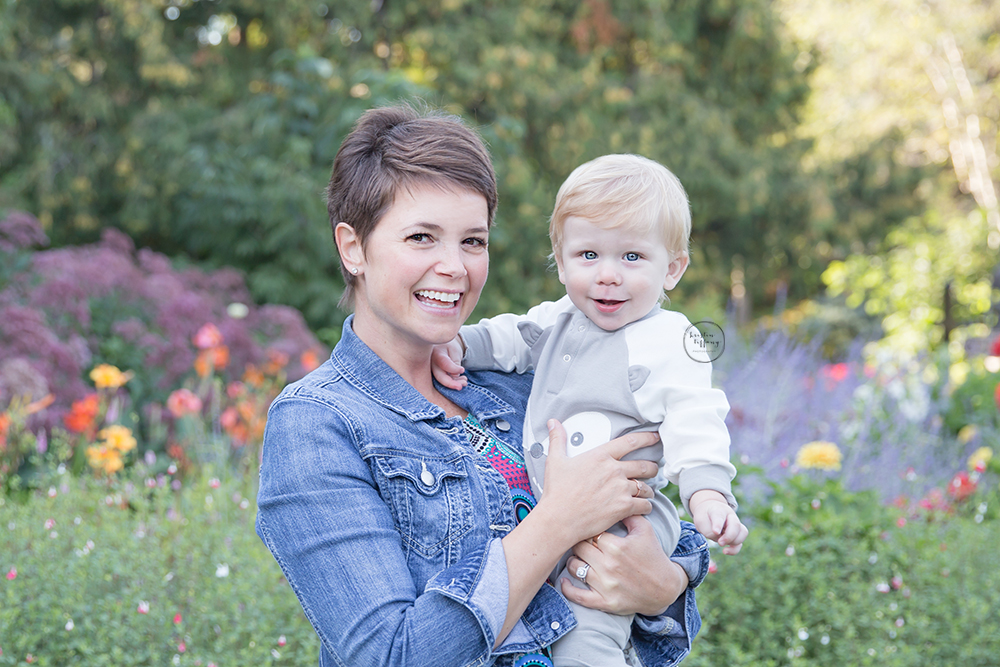 a photo of a mother holding her baby son by a flower garden