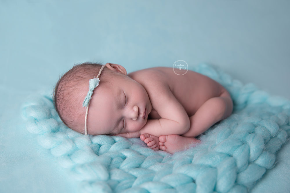 a photo of a newborn baby girl posed on a knit blanket