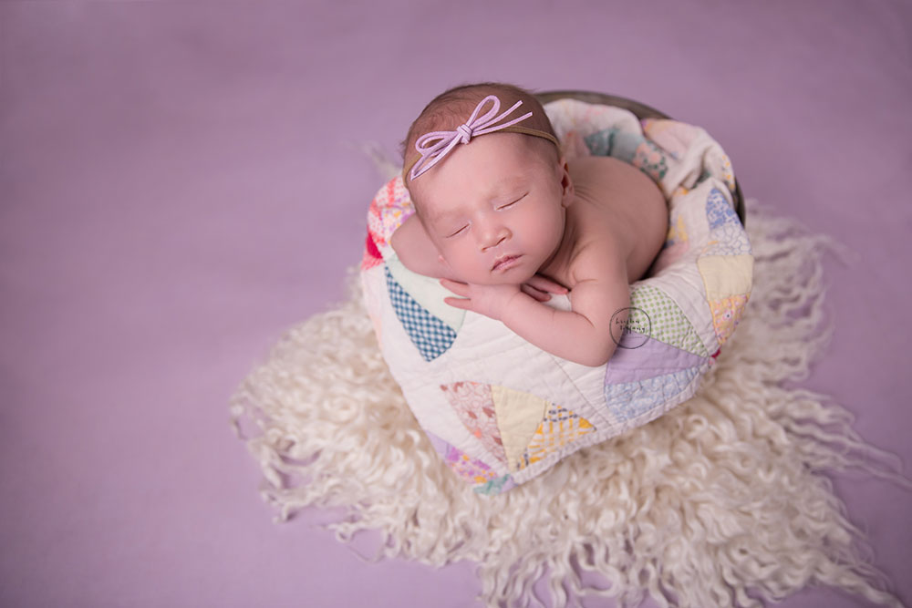 a photo of a newborn baby girl posed in a bucket with a quilt