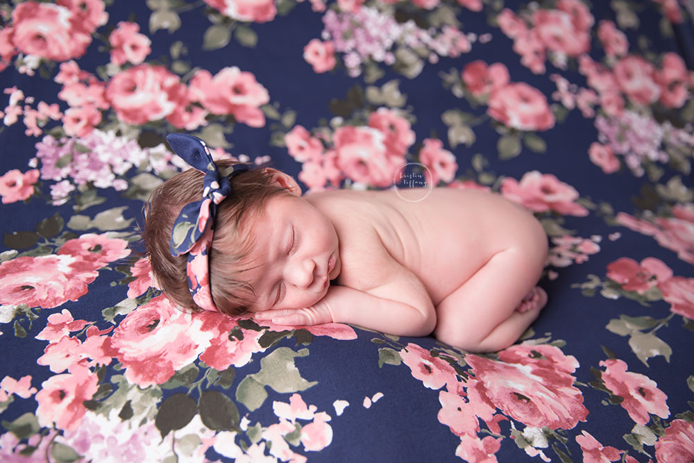 a photo of a posed newborn baby girl on floral fabric