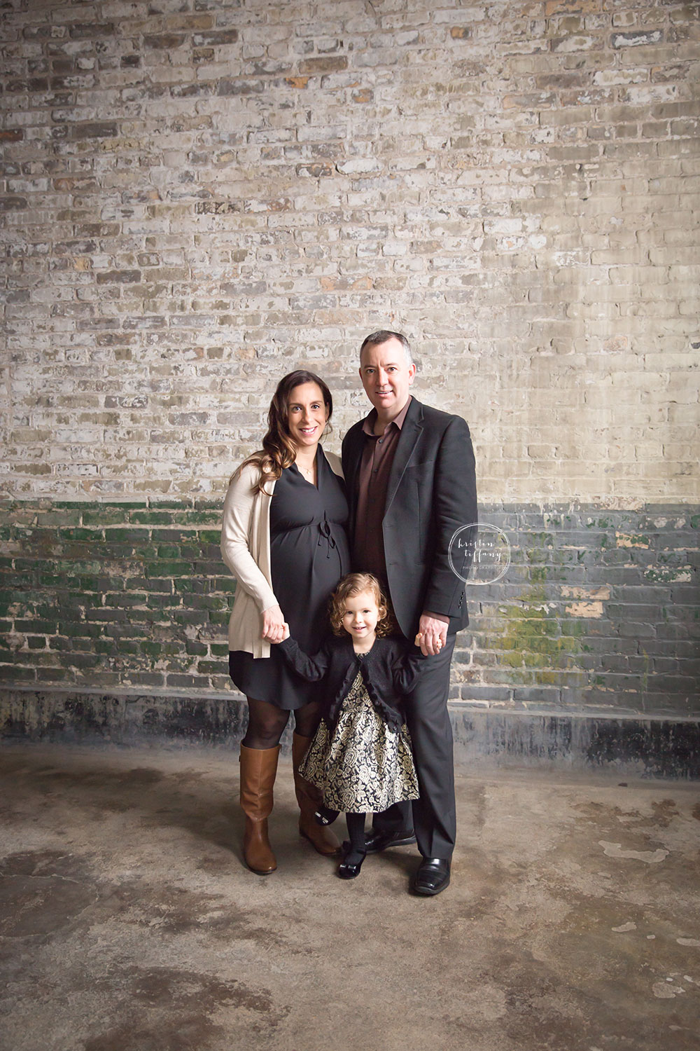 a family maternity photo by a distressed brick wall