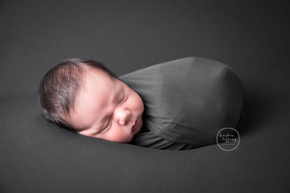 a photo of a swaddled newborn baby boy in grey