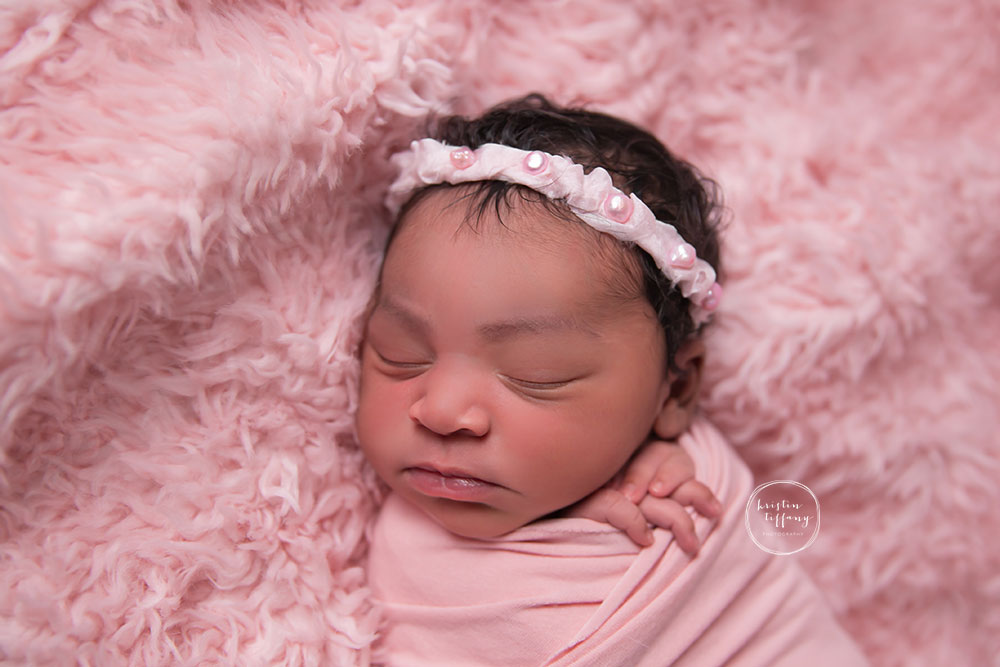 a newborn photo of a baby girl sleeping in pink faux fur