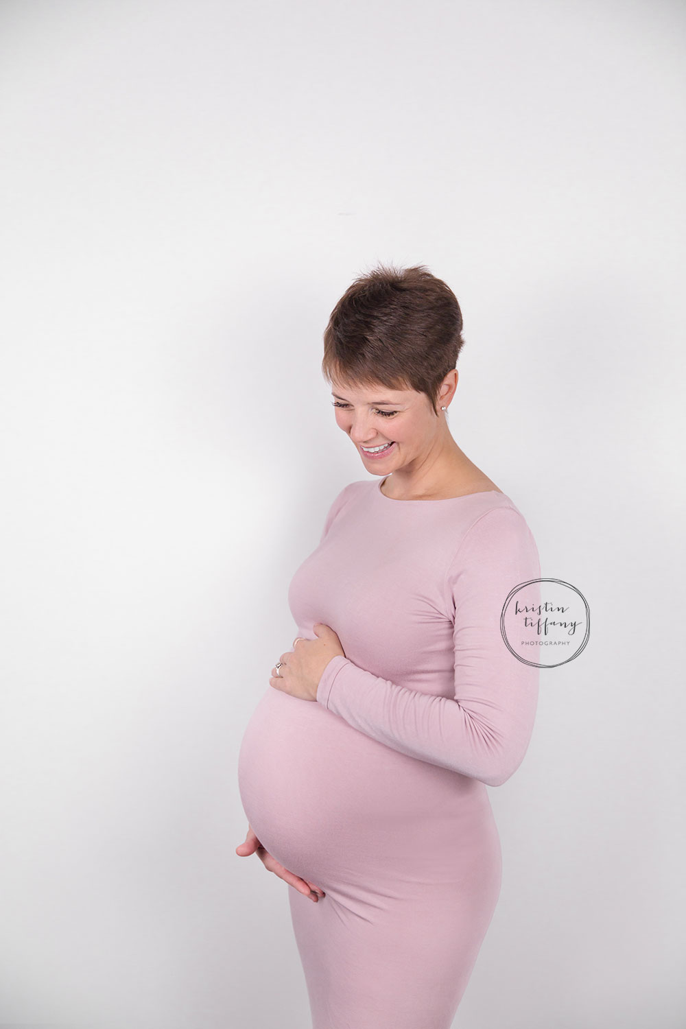 a maternity photo of a woman smiling in a pink dress