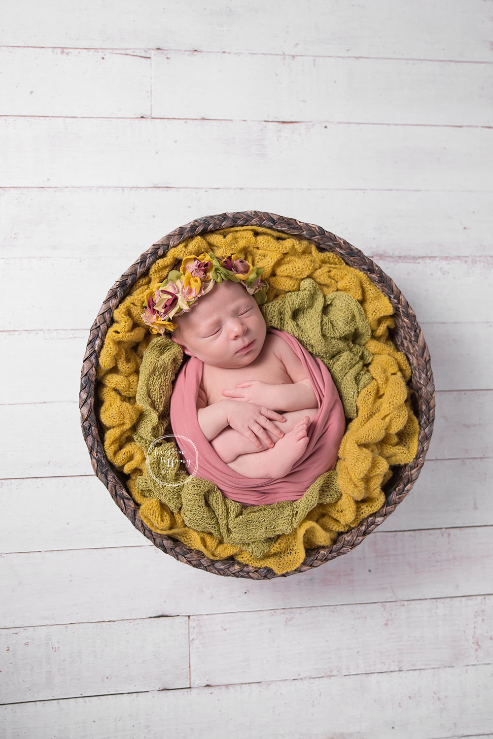 a photo of a newborn baby girl in a basket wearing a floral halo