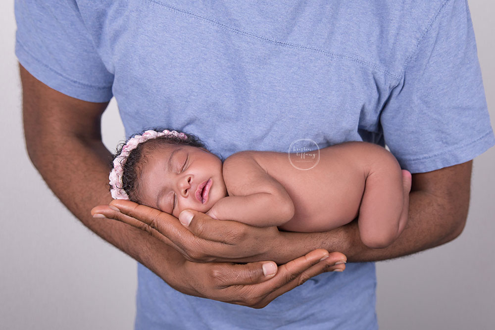 a photo of a newborn baby girl in her dad's arms at a posed newborn session