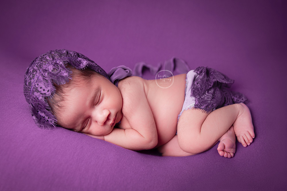 a newborn photo of a sleeping baby girl in a purple outfit