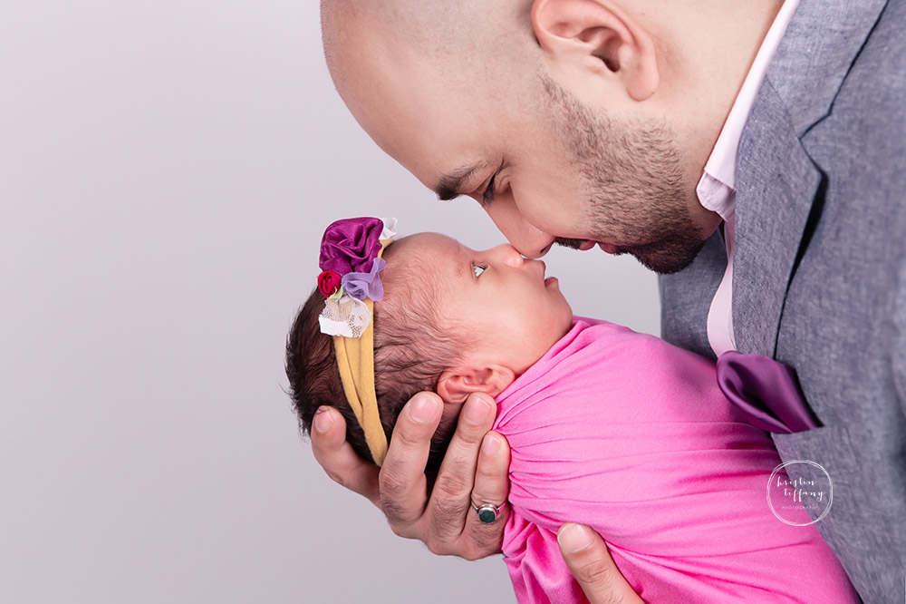 a newborn photo of a baby girl and her dad touching noses