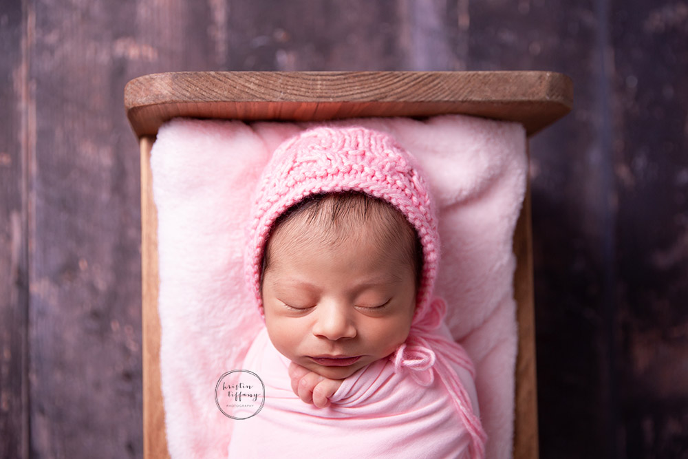 a newborn photo of a baby girl sleeping in a wooden bed