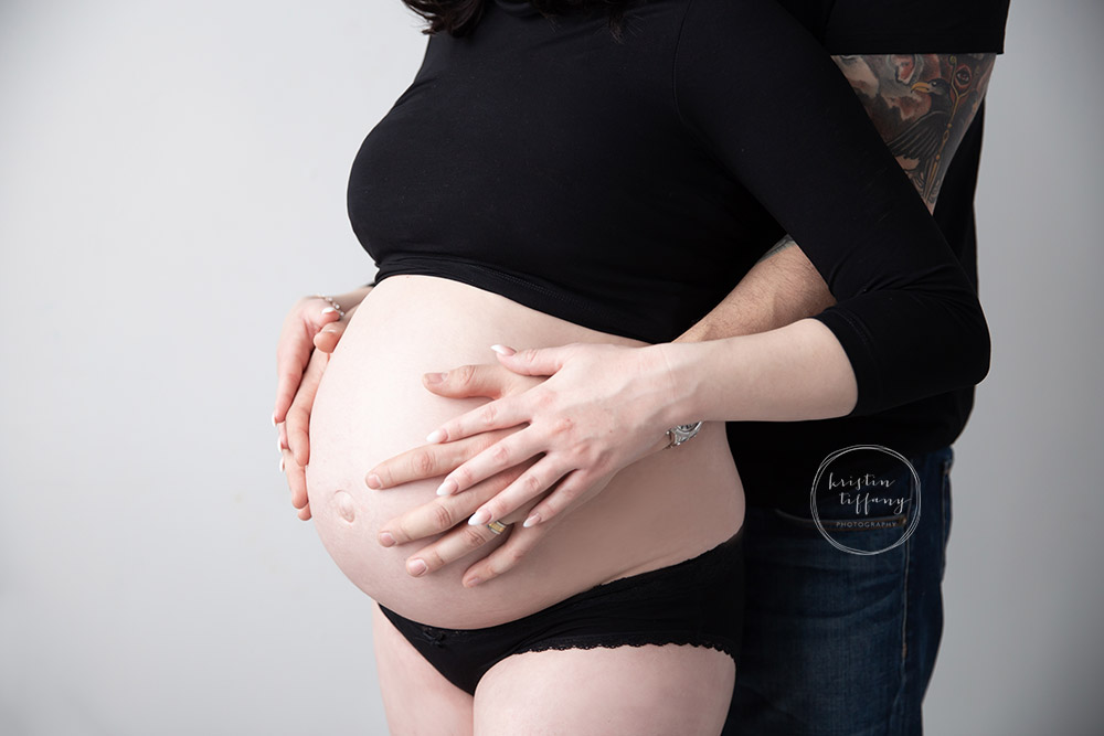 a maternity photo of a husband and wife holding her belly