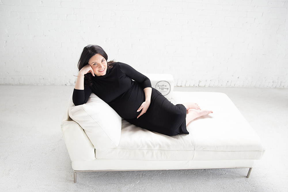 a maternity photo of a woman lying on a white leather couch