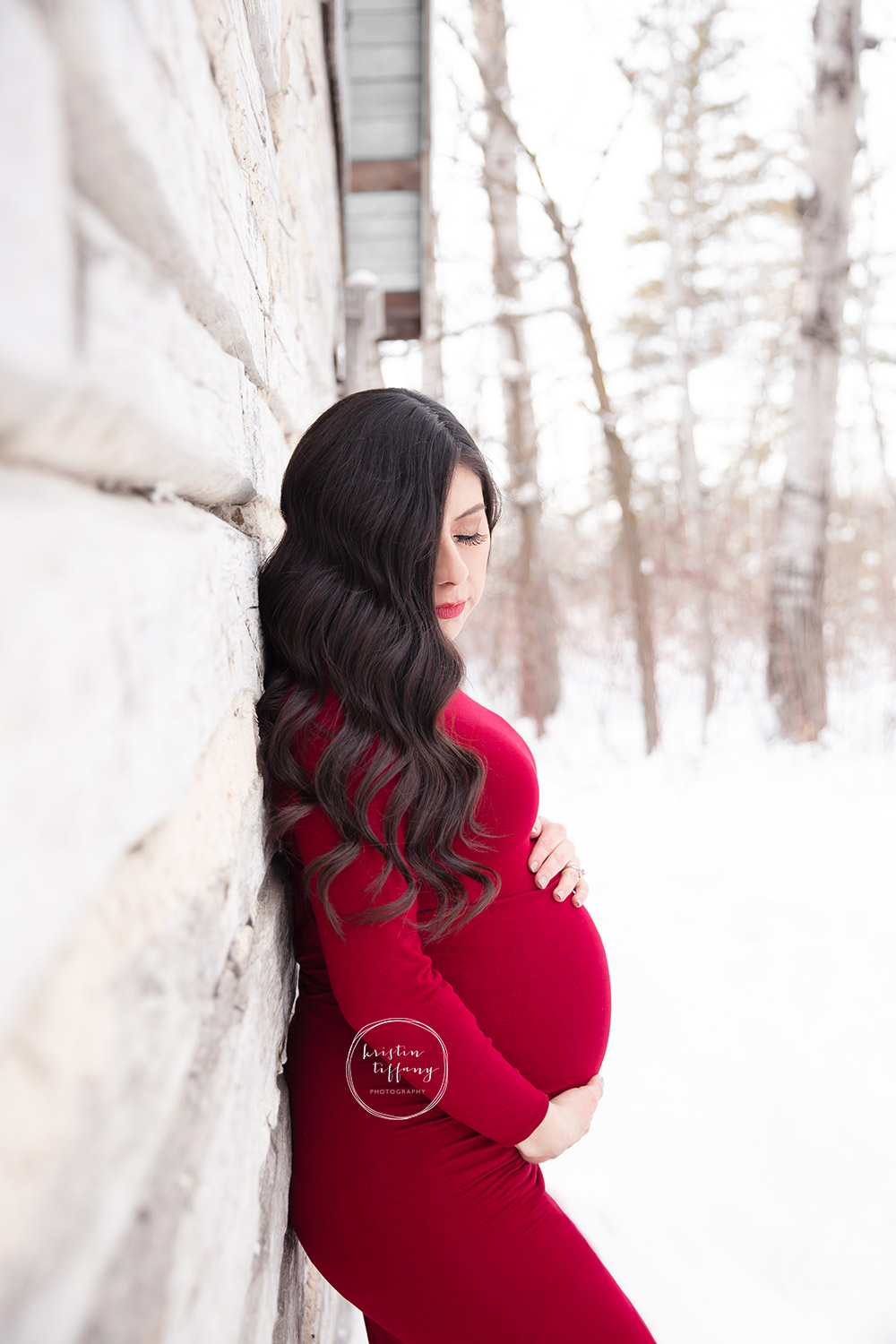 a maternity photo of a woman wearing a red gown in the snow
