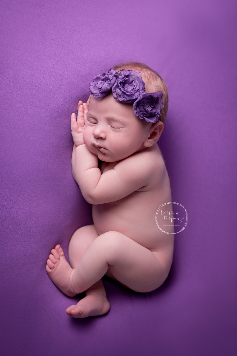 a newborn photo of a baby girl sleeping on a purple backdrop