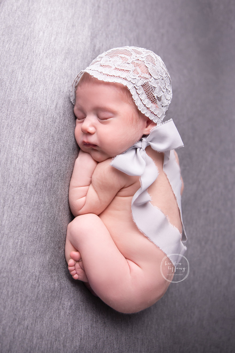 a photo of a newborn baby girl posed on a grey backdrop