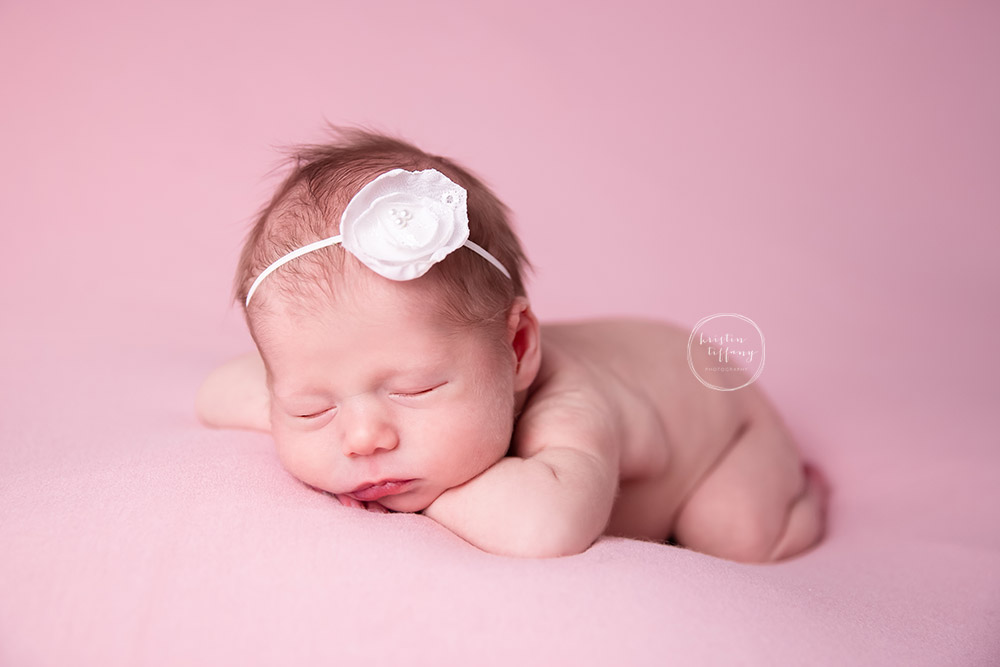 a newborn photo of a baby girl posed on pink fabric